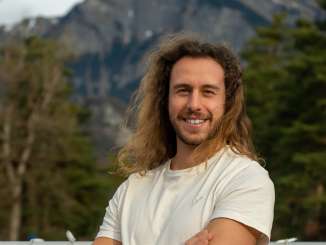 Young man with long brown hair smiles at the camera