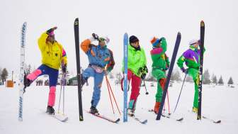 Five men in retro ski suits and old skis pose on the slopes of Flumserberg