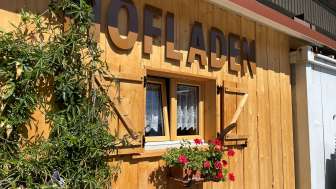 A wooden hut with flowers and the inscription "Hofladen" (farm store)