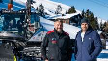 Pistenbully driver Peter Thut stands with presenter Manuel Rothmund in front of Pistenbully in the snow
