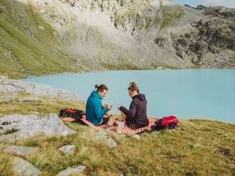 Couple sitting on a picnic blanket in front of an ice-blue mountain lake