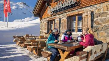 Three friends enjoy coffee on the sun terrace of the Gruebhütte