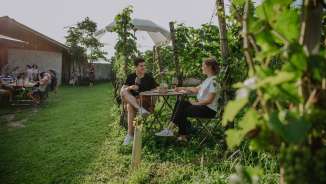 Two people sit among the vines and enjoy a glass of wine together.